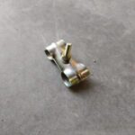Small metallic clamp with threaded bolts resting on a concrete floor