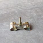 Small metal pipe clamp with a vertical bolt on a gray concrete floor.