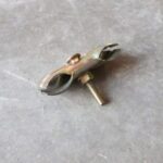 Small metal clamp-like tool with two curved jaws and a threaded stud resting on a concrete floor.